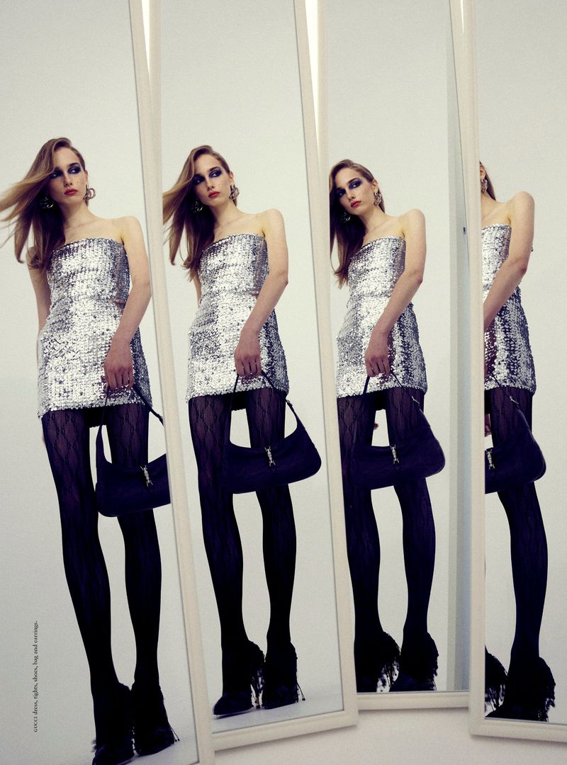 Model Audrey Lees wearing a silver sequin strapless dress and black patterned tights, reflected in multiple standing mirrors.
