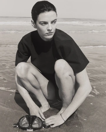 Model Beauïse Genç crouching on a wet sandy beach next to a diving mask in black and white for Numéro France.