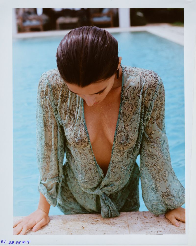 Anna Pricope in a sheer patterned green cover-up top leaning on the edge of a swimming pool.