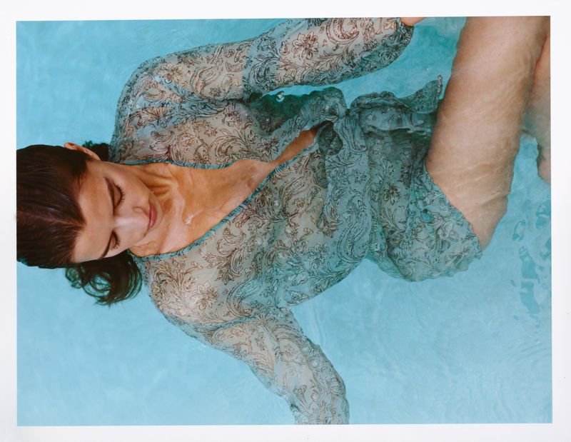 Model floating in clear blue pool water wearing a semi-sheer sage green paisley patterned cover-up.
