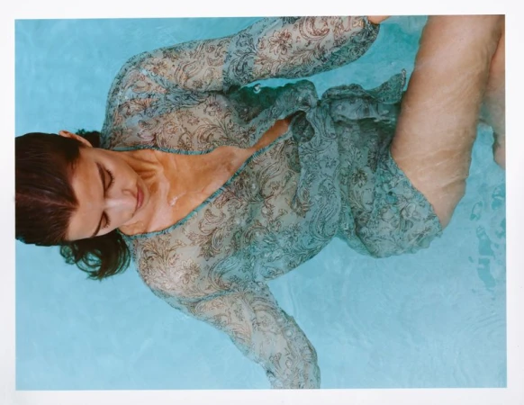 Model floating in clear blue pool water wearing a semi-sheer sage green paisley patterned cover-up.