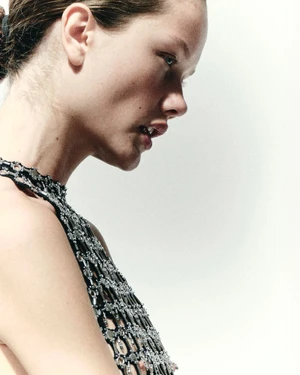 Model in profile wearing a metallic chainmail halter top against a plain white background.