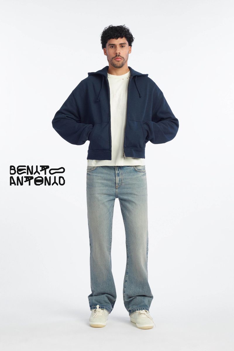 Bernie Martinez standing against a white seamless backdrop wearing a navy zip jacket and light wash jeans for Zara Benito Antonio.
