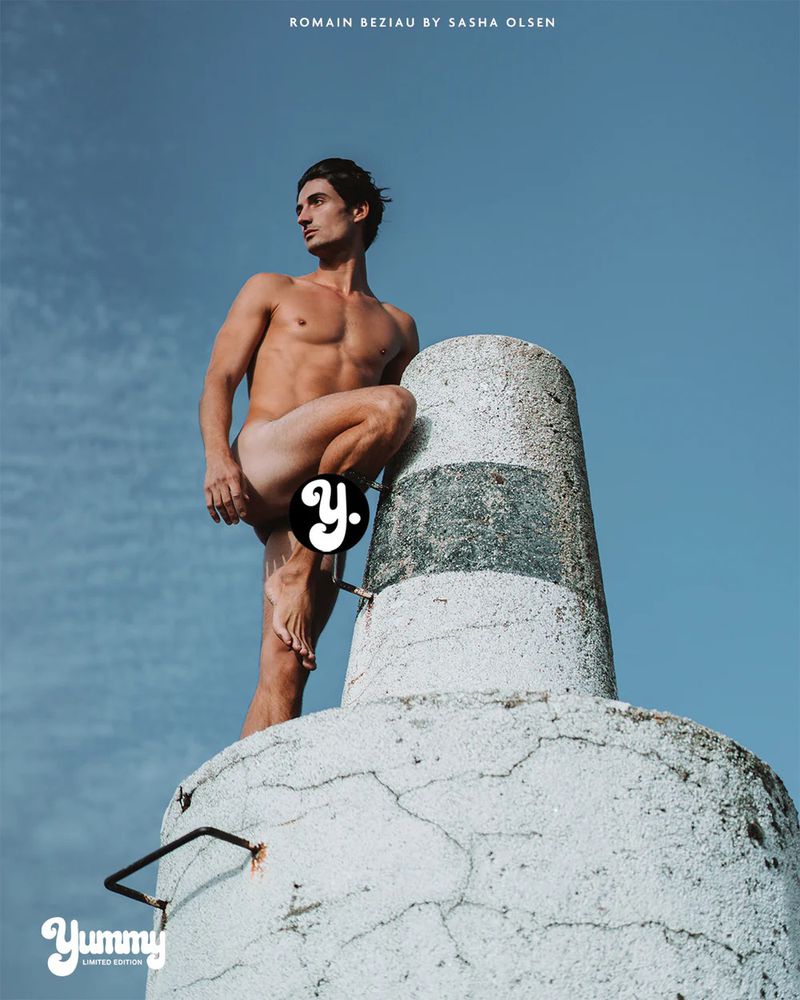 Romain Beziau poses nude on a weathered concrete maritime pillar against a clear blue sky, photographed by Sasha Olsen for Yummy.