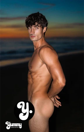 Romain Beziau standing in profile on a sandy beach at dusk with hands behind his back, photographed for Yummy.