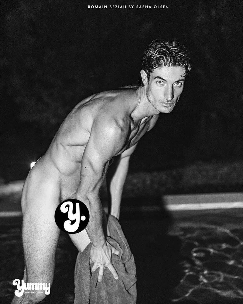 Black and white photo of model Romain Beziau leaning forward poolside at night while holding a towel.