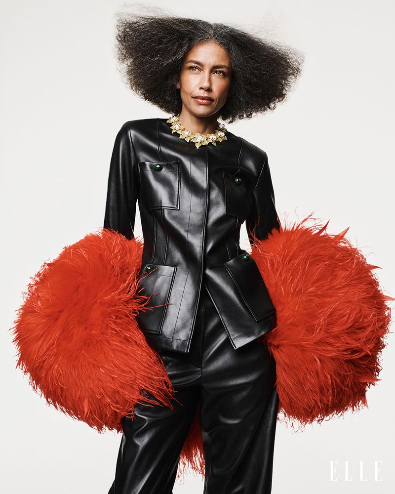 Model Stephanie Cavalli in a black leather jacket with voluminous red feather sleeves against a white backdrop.