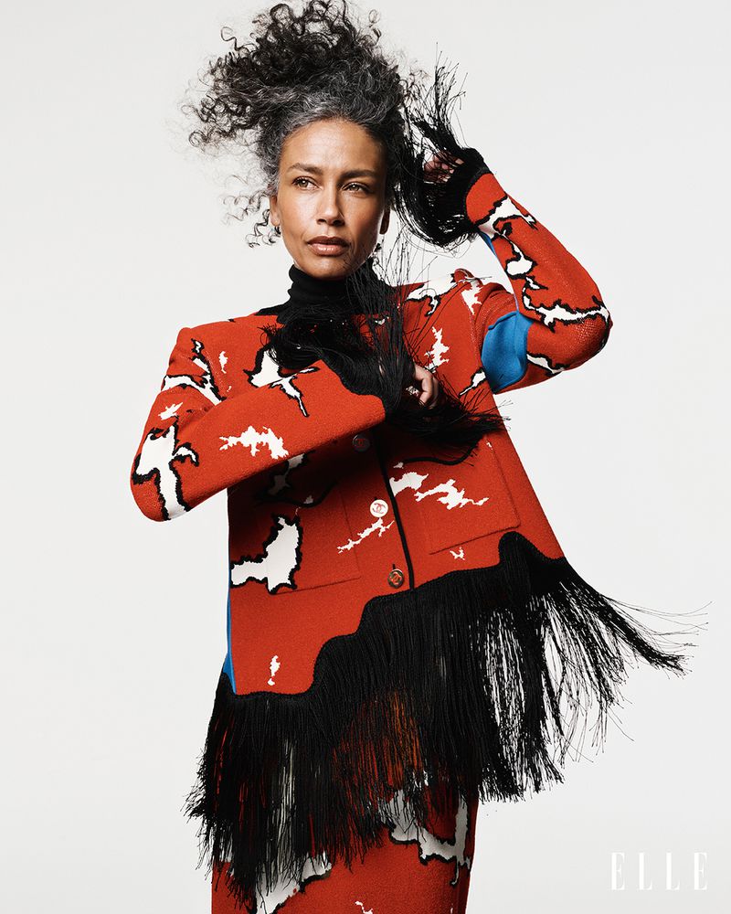 Stephanie Cavalli wearing a red and black patterned fringe jacket against a white studio backdrop for Elle Brasil.