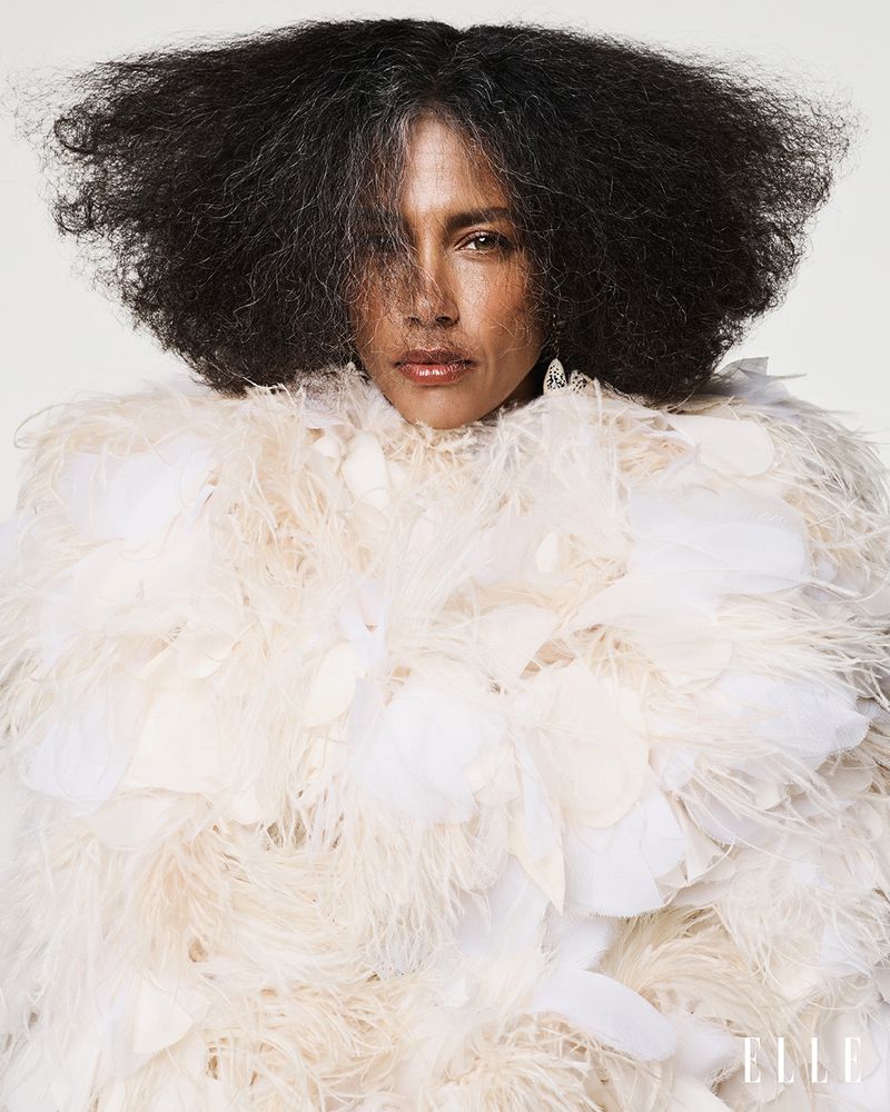 Model Stephanie Cavalli in a voluminous cream feather coat with expansive dark hair facing forward against a white studio background.