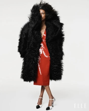 Model Stephanie Cavalli in a voluminous black shaggy coat and red sequin dress against a white studio background for Elle Brasil.