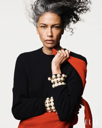 Model Stephanie Cavalli in a black sweater and red wrap wearing chunky pearl cuff bracelets against a white background.