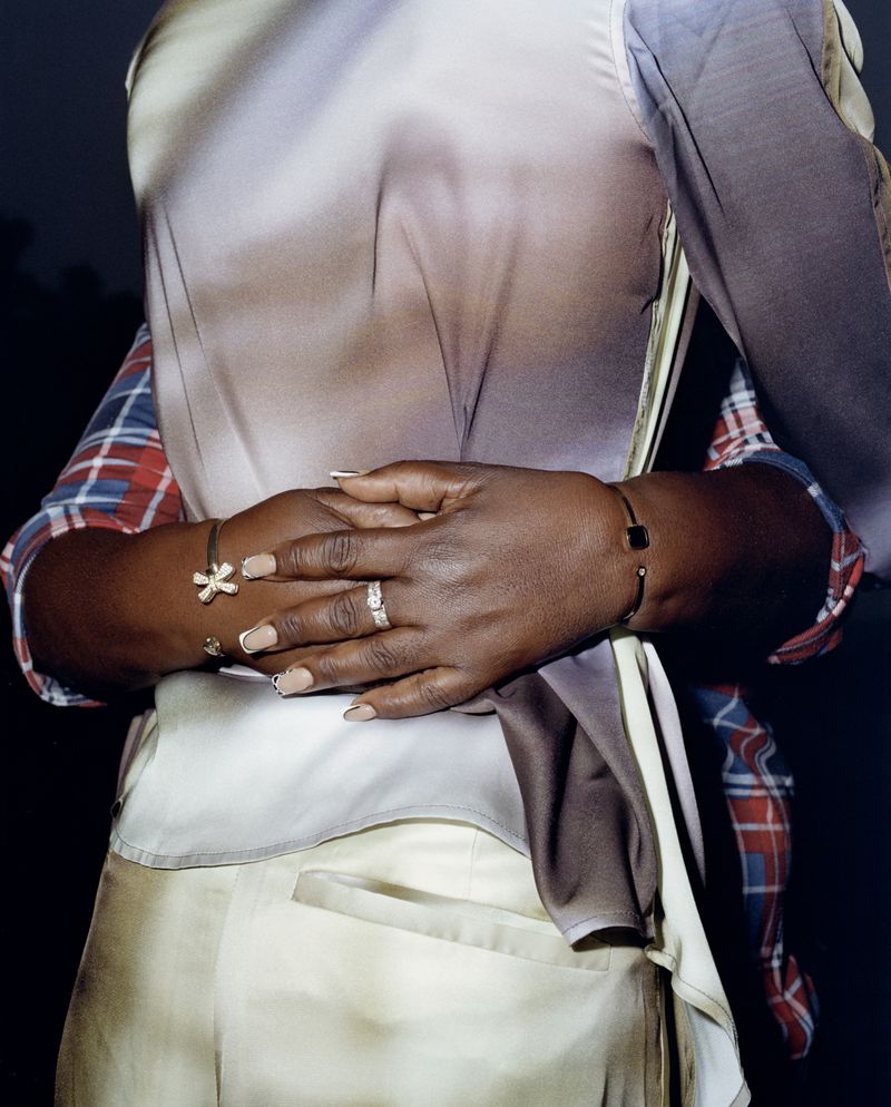 Close-up shot of an adult woman's arms wrapped around her body, wearing a stylish layered shirt and jewelry, showcasing fashion details.