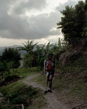 Man standing on an outdoor dirt path beneath a cloudy sky, wearing patterned shirt and trousers for Bianca Saunders 38 Love Lane.