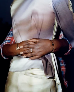 Close-up of hands with cuff bracelets clasped over a draped ombre silk shirt with plaid sleeves wrapping from behind.