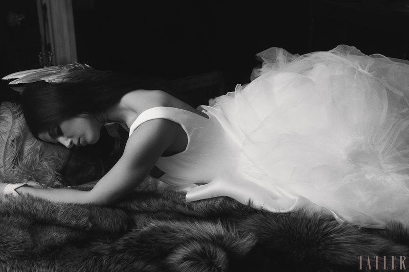 Monochrome portrait of woman in white gown reclining on fur, bathed in soft light, highlighting the texture of fabric and fur.