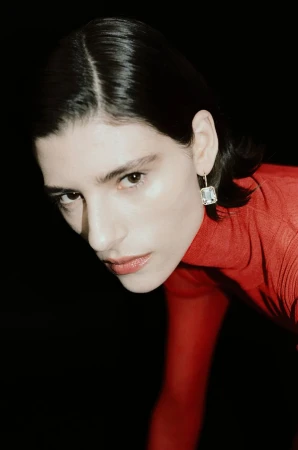 Model wearing a sparkling rectangular crystal drop earring and a fitted red sheer top against a solid black background.