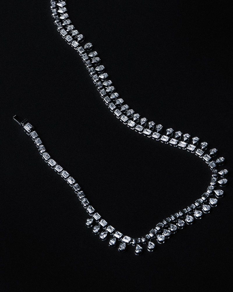 Diamond necklace with emerald-cut and teardrop stones arranged on a solid black background.