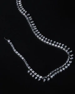Diamond necklace with emerald-cut and teardrop stones arranged on a solid black background.