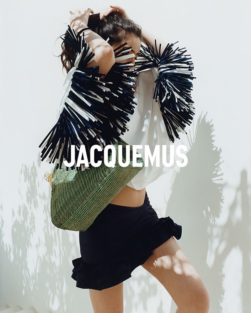 Model Isis Bensalem posing in a fringe-sleeve top, black ruffled skirt, and green woven tote bag for Jacquemus.
