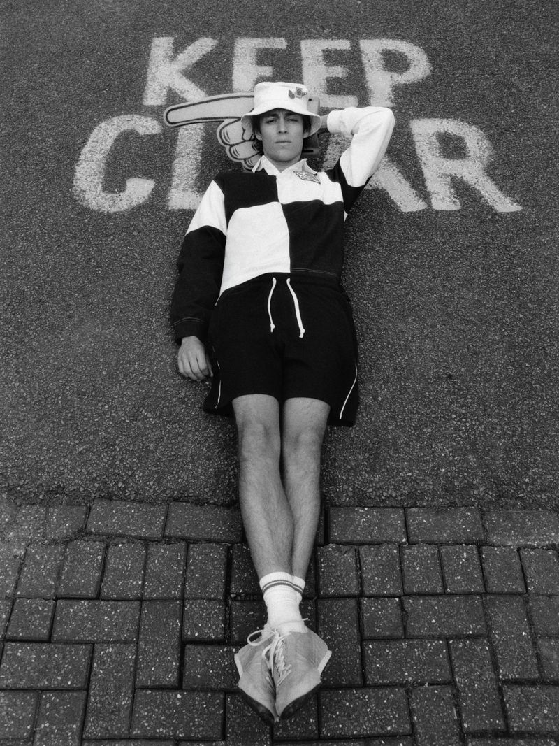 Man in a bucket hat and checkered shirt lying on pavement with Keep Clear road markings