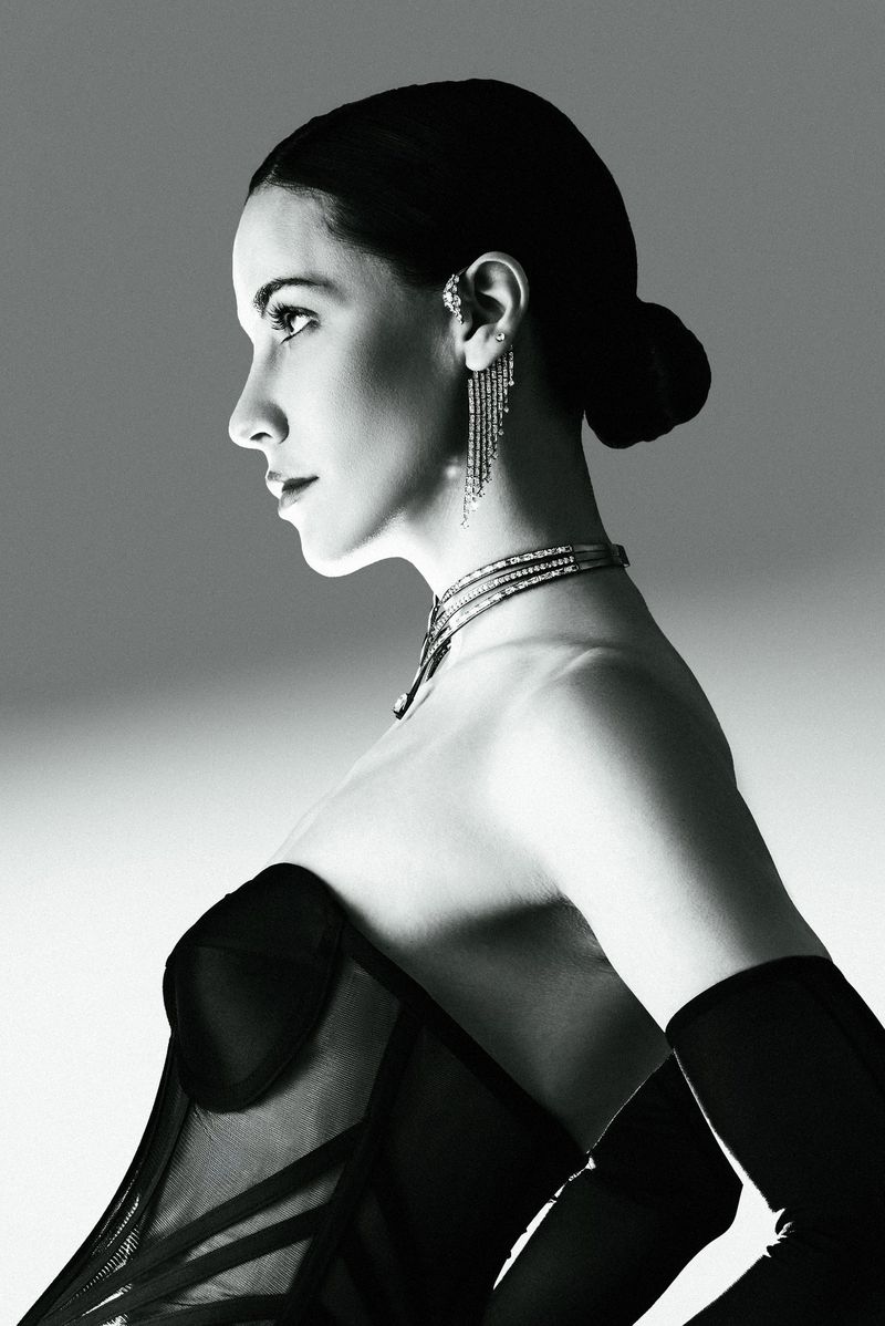 Monochrome profile portrait of model Anna Alimani wearing a black corset, opera gloves, and diamond jewelry against a studio backdrop.