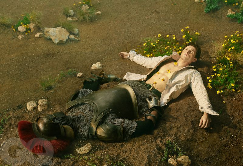 Tom Holland lying on dirt with yellow flowers beside a suit of armor for GQ Magazine U.S.