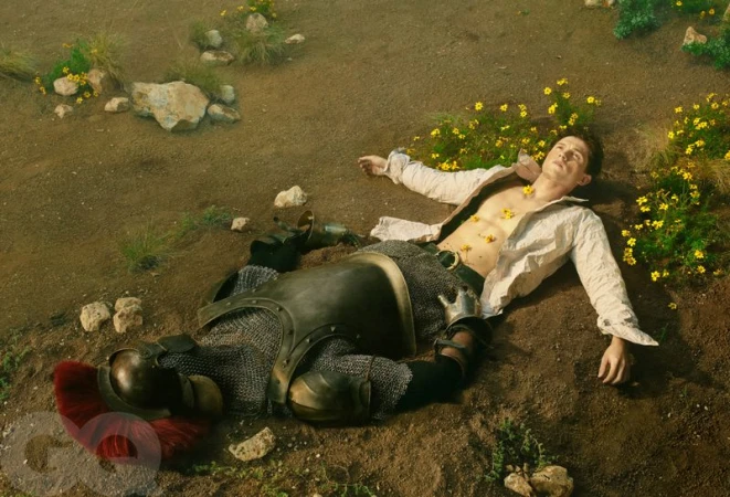 Tom Holland lying on dirt with yellow flowers beside a suit of armor for GQ Magazine U.S.