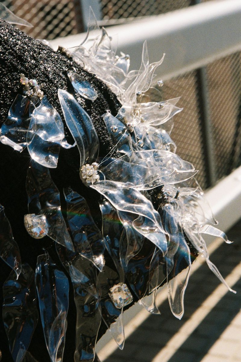 Close-up detail of a textured black garment adorned with sculpted clear plastic fringe and sparkling crystal embellishments.
