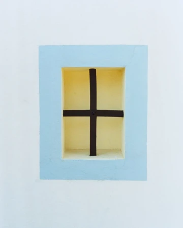 Architectural window detail with a light blue frame, dark cross bar, and pale yellow niche on a white wall.