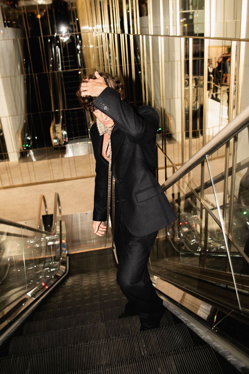 Man wearing a dark suit descending an escalator in a modern interior setting