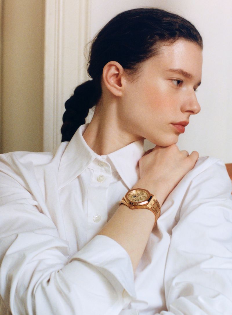 Model Sandra Murray wearing a crisp white collared shirt and a gold wristwatch with her braided hair pulled back.