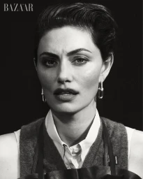 Black and white portrait of Phoebe Tonkin with slicked-back hair wearing a collared shirt, knit vest, and link earrings.