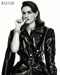 Phoebe Tonkin wearing a belted black leather trench coat and silver chain jewelry against a white studio background.