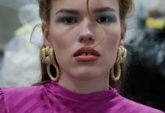 Close-up portrait of model Mathilde Lakjaer wearing chunky gold door-knocker earrings and a bright magenta top.