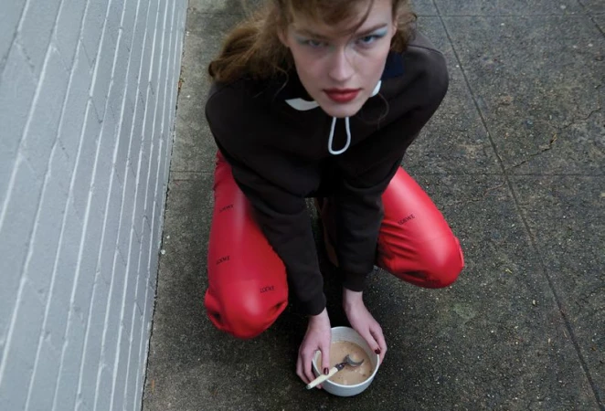 Mathilde Lakjaer crouching on pavement in a brown hoodie and bright red balloon pants next to a white bowl for Russh.