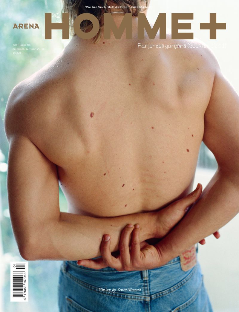 Shirtless man seen from behind with arms clasped at his lower back wearing blue jeans on the Arena Homme+ magazine cover.