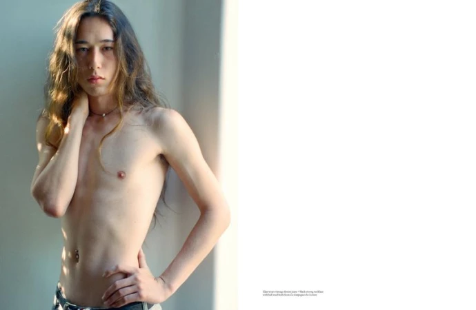 Shirtless male model with long wavy hair posing in a minimal studio setting for an Arena Homme + editorial spread.