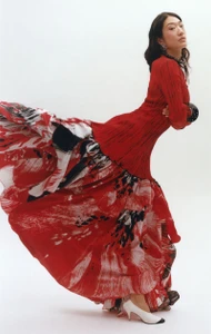 East Asian woman posing in a billowing red dress with an abstract brushstroke print and white heels against a white backdrop.