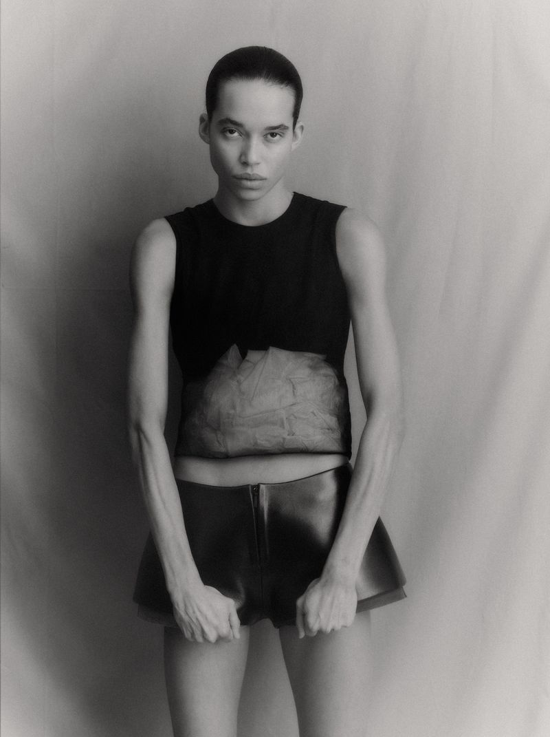 Model in a black sleeveless top and dark shorts against a textured neutral studio backdrop