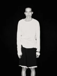 Lara Menezes wearing a white long-sleeve shirt and black shorts against a solid black background.