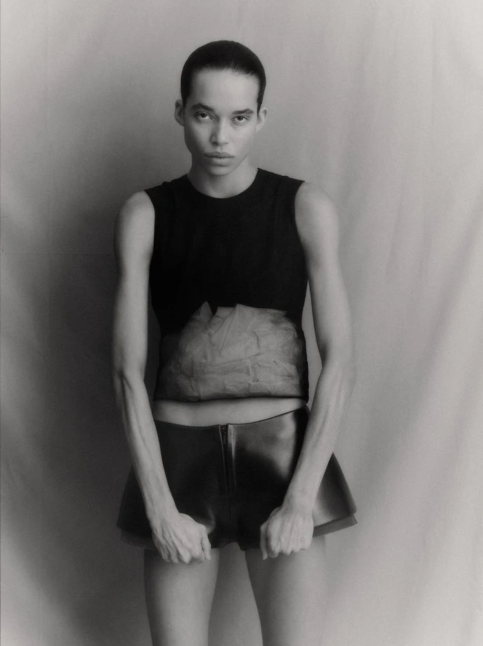 Model in a black sleeveless top and dark shorts against a textured neutral studio backdrop