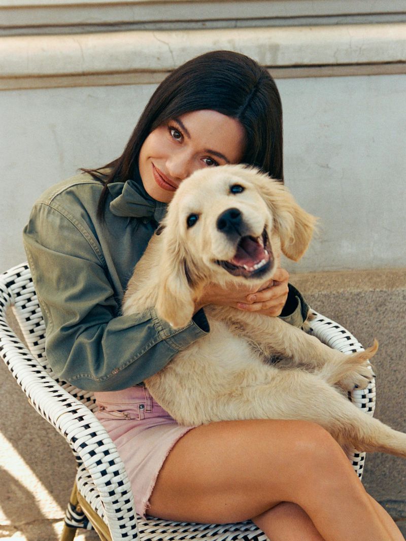 Anna Castillo seated in a woven chair holding a golden retriever puppy outdoors.
