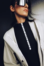 Model wearing oversized sunglasses, a black zipped top, and a light-coloured jacket for the Athletica project by Aje.