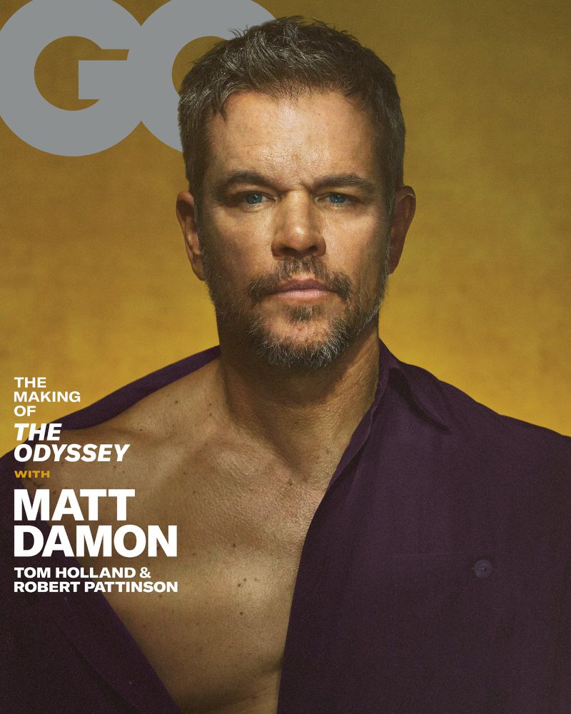 Matt Damon wearing an unbuttoned dark purple shirt against a warm golden backdrop for a GQ Magazine cover.