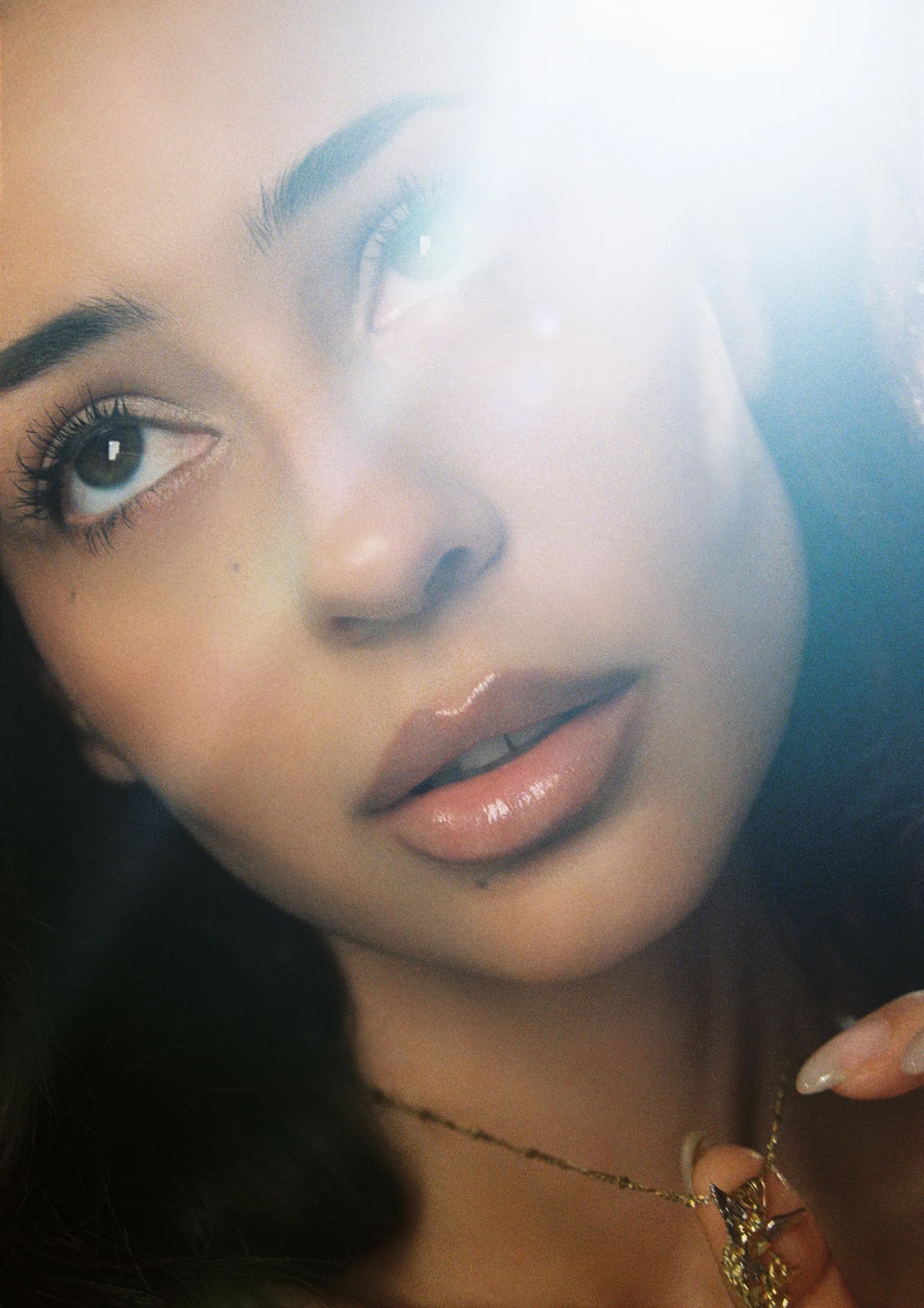 Close-up beauty portrait of Alexa Demie with glossy lips and gold necklace under soft lens flare.
