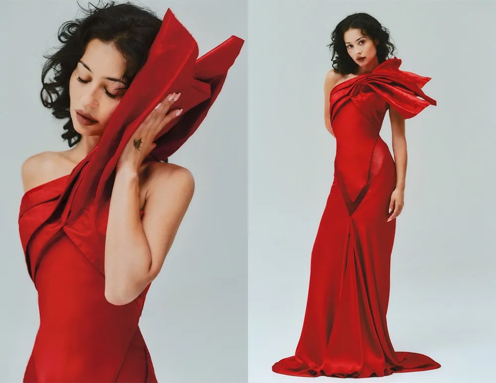 Alexa Demie wearing a red one-shoulder gown with sculptural detailing against a plain light background