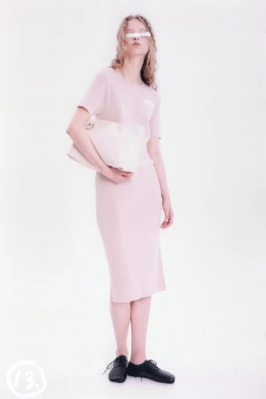 Full-length studio shot of a young adult woman in a peach dress with a clutch, black shoes, and white bar covering her eyes.
