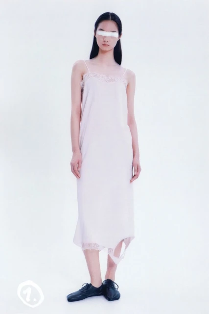 Studio shot of an Asian female model posing in a white slip dress and black dress shoes against a clean white backdrop.