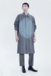 Model wearing a grey faded gradient long coat, grey trousers, and black square-toe boots against a white studio background.