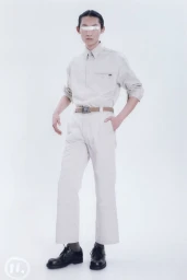 East Asian male model wearing a beige collared shirt, matching trousers, and black dress shoes with white tape over eyes.
